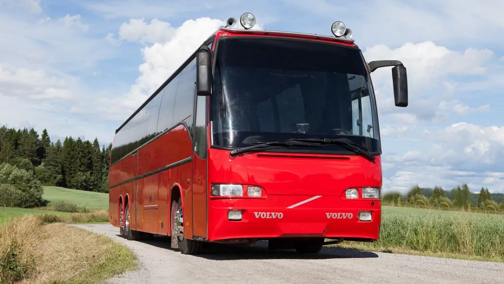 En skinnende rød Volvo turbuss parkert på en grusvei under en skyfri himmel