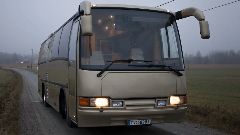 Gullfarget turbuss sett forfra på en grusvei i tåkete vær.