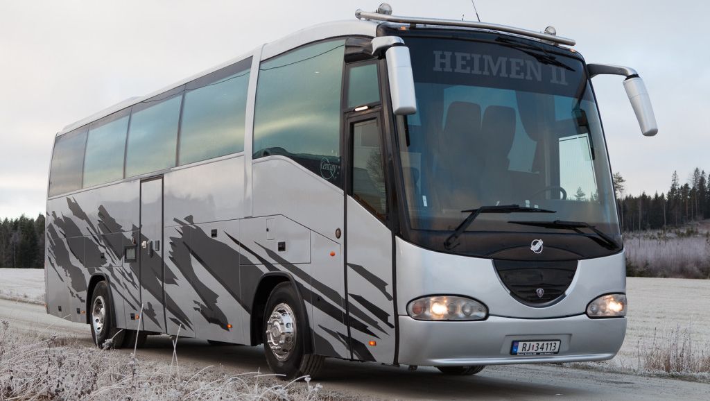 Fronten av en sølvfarget buss med "HEIMEN II" på frontruten, parkert på en frostbelagt vei.