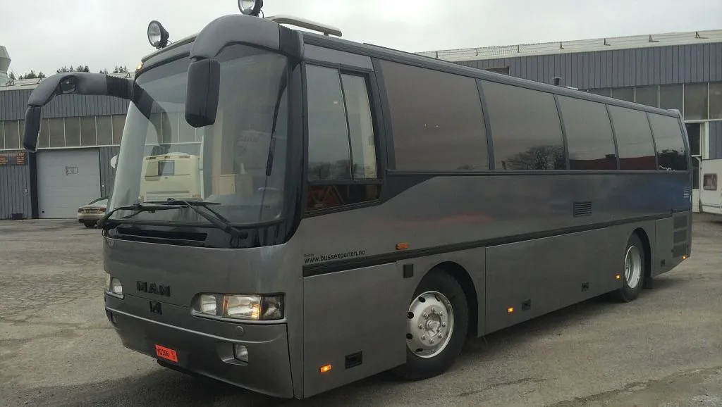 Grå MAN turbuss med sotede ruter sett skrått forfra fra høyre side.