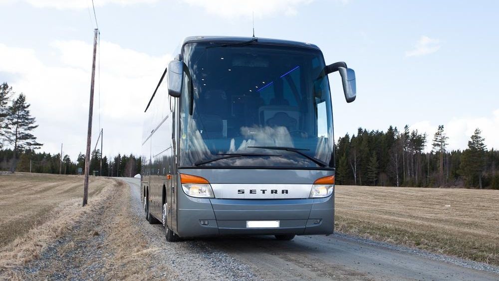 Fronten av en grå Setra turbuss parkert på en grusvei i et landlig område