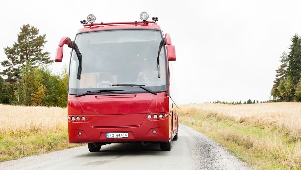 Fronten av en rød buss på en grusvei i et landskap med jorder og trær.