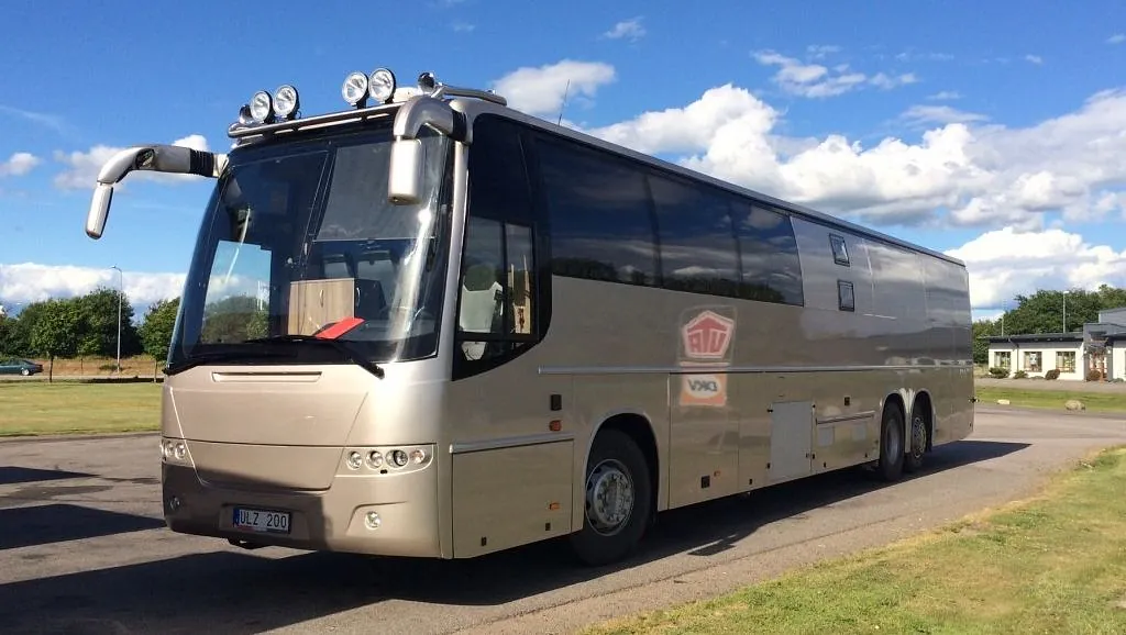 Lys og varm grå buss står parkert på asfalt med gress rundt