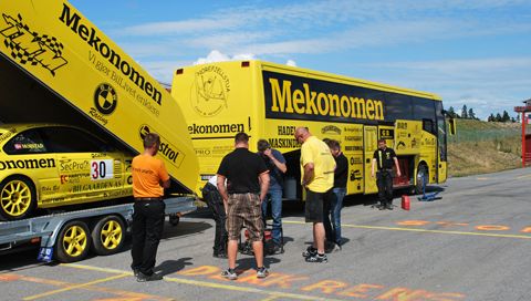 Folk samles ved gul Mekonomen-buss og tilhenger med racerbilen lastet bakpå.