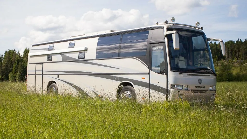 Scania turbuss parkert i gresseng, med mørke vinduer og strømlinjeformet design.