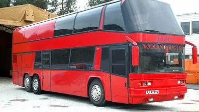 Stor rød dobbeltdekkerbuss parkert ute, med mørke vinduer og teksten "Nodland Racing."