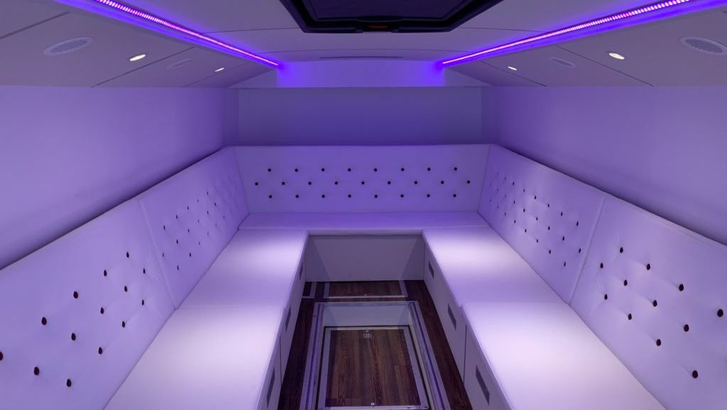 U-formet lounge i hvitt polstret skinn blir opplyst av lilla lyslister i tak