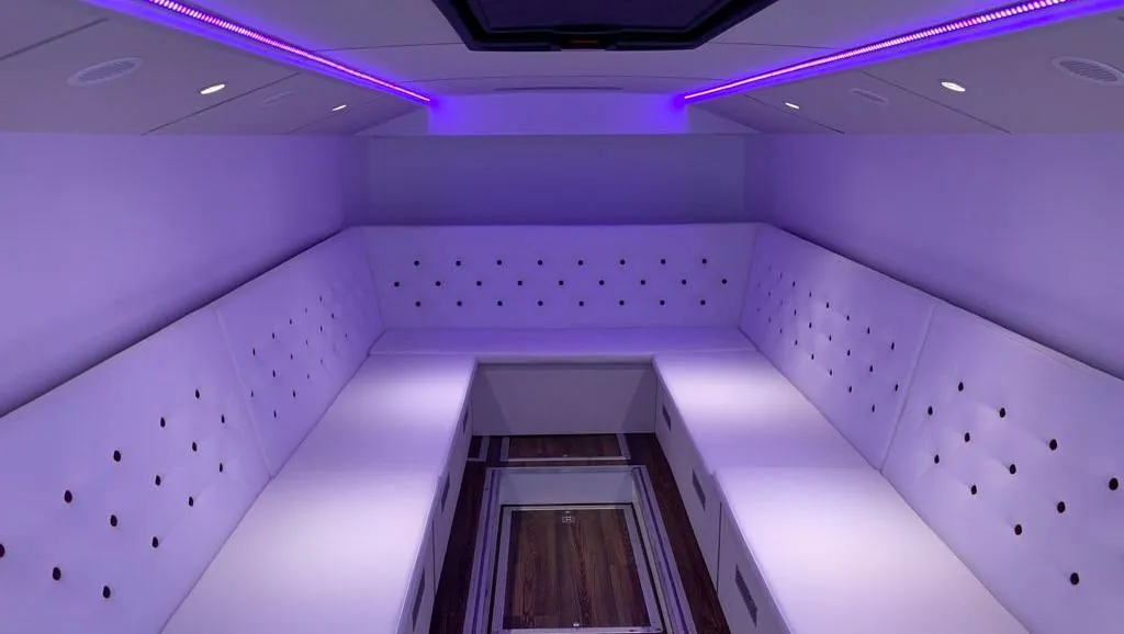 U-formet lounge i hvitt polstret skinn blir opplyst av lilla lyslister i tak