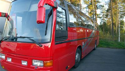 Rød turbuss sett fra siden og front, parkert ved vei omgitt av trær.