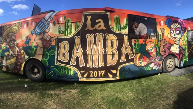 Sidevisning av buss med tegneserieaktig lakkering og stor "La Bamba 2017"-logo.