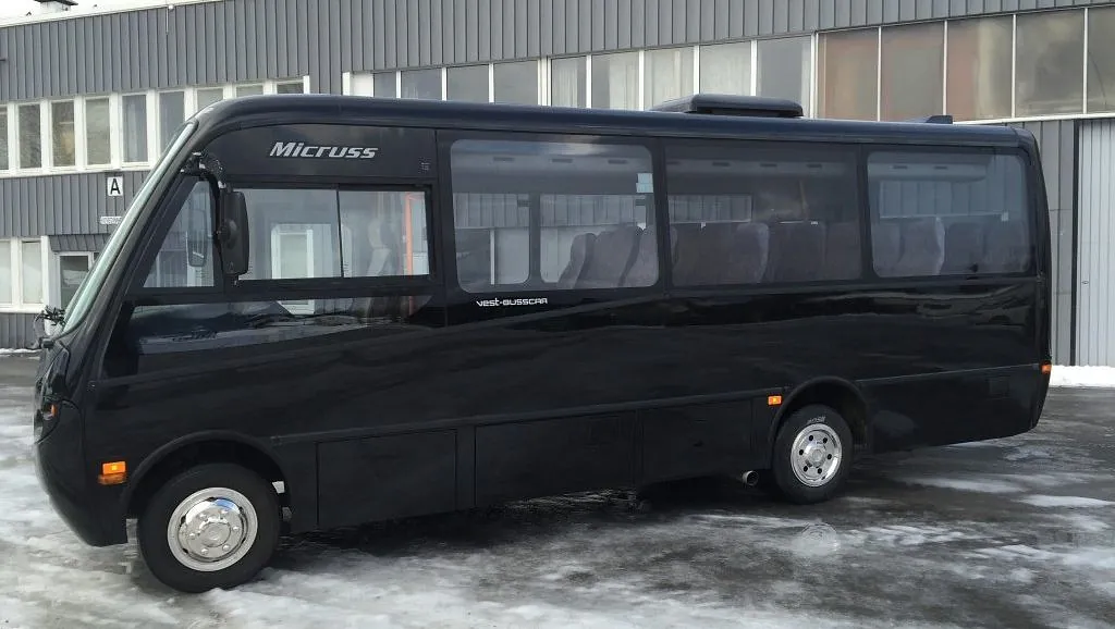 En svart Micruss minibuss parkert på et snødekt område foran en industribygning